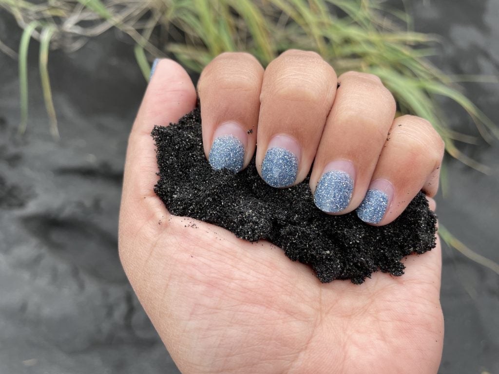 A hand with glittery blue nails holding a handful of sparkling black sand.