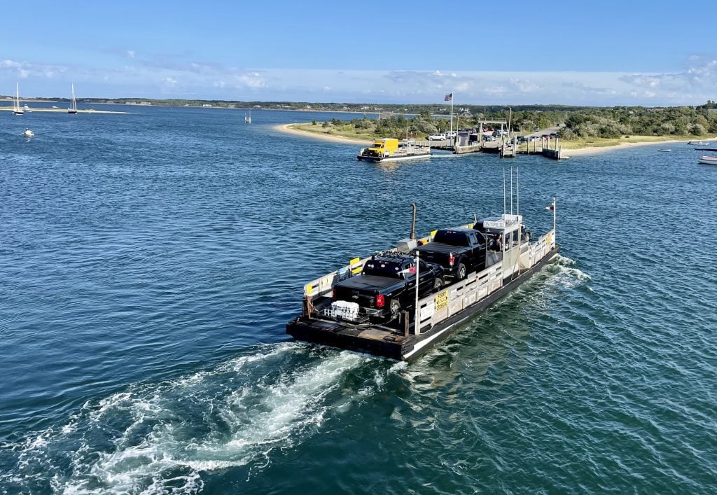 A teeny tiny ferry that just barely fits three cars crossing a channel to an island.