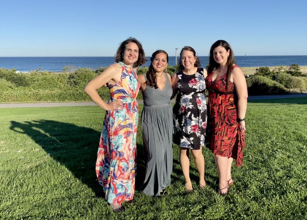 Kate and her three best female friends wearing formal dresses and standing on a lawn with the ocean in the distance behind them.