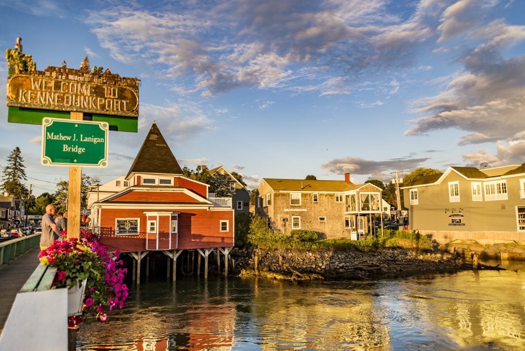 A bridge leading to a town filled with clapboard houses on the water.