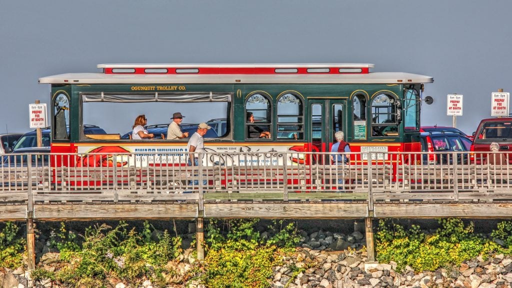 A bright orange and green trolley driving over a wooden bridge.