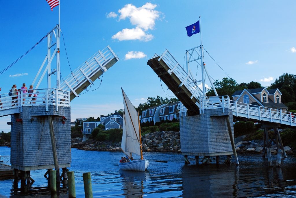 A sailboat sails between sides of a bridge in Ogunquit.