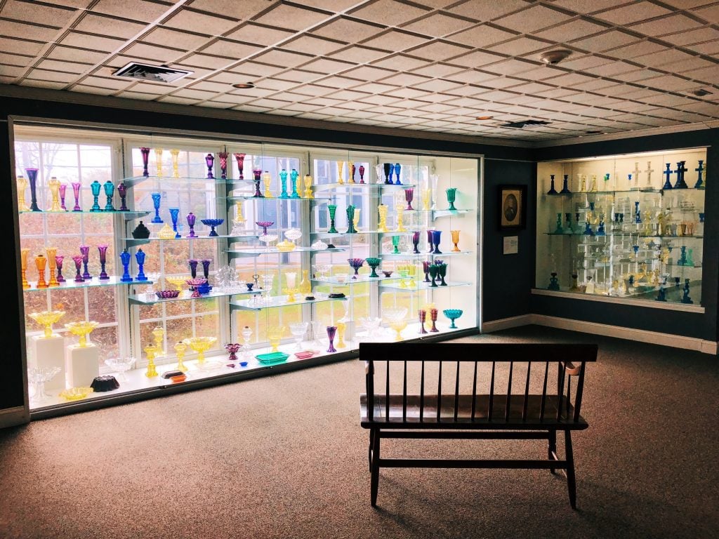 A museum room with a big glass case filled with brightly covered vases.