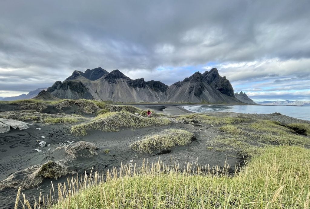 Endless hills of black sand dunes topped with green grasses, and in the background, a jagged black mountain.