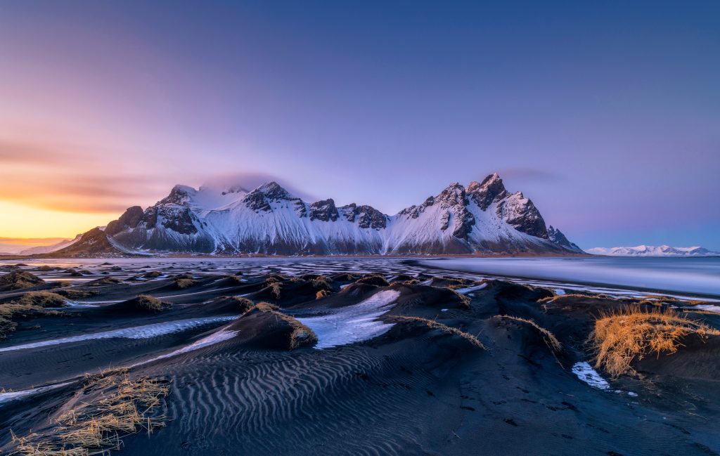 Spiky Vestrahorn mountain underneath a dusting of snow and a purple sky.