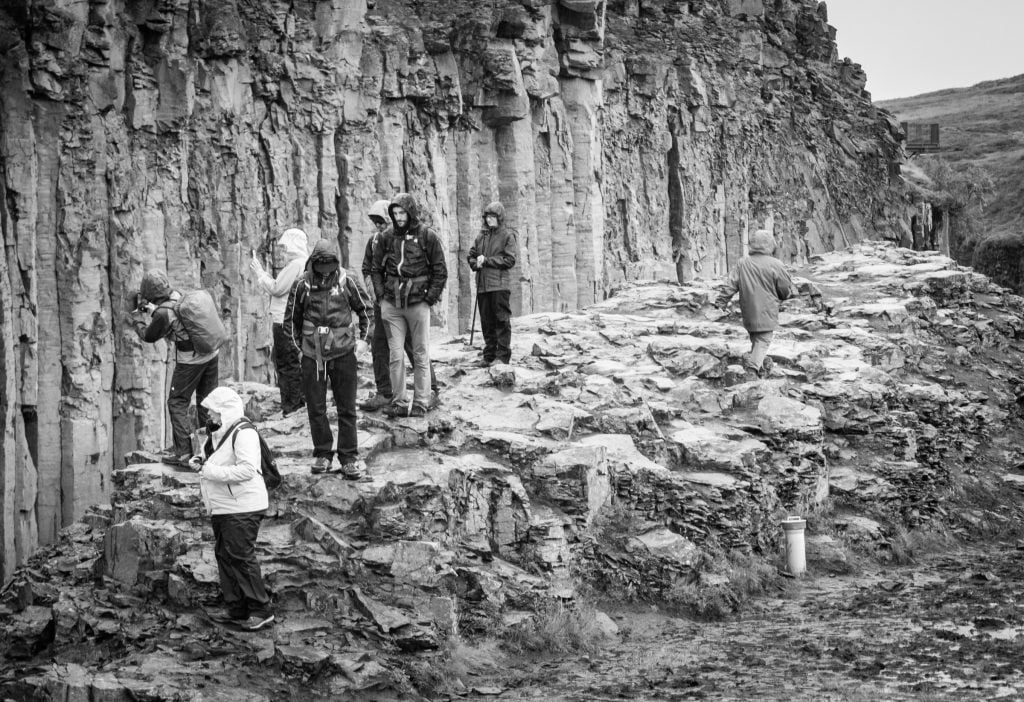 A black and white shot of hooded hikers in the rain taking photos of the canyon.