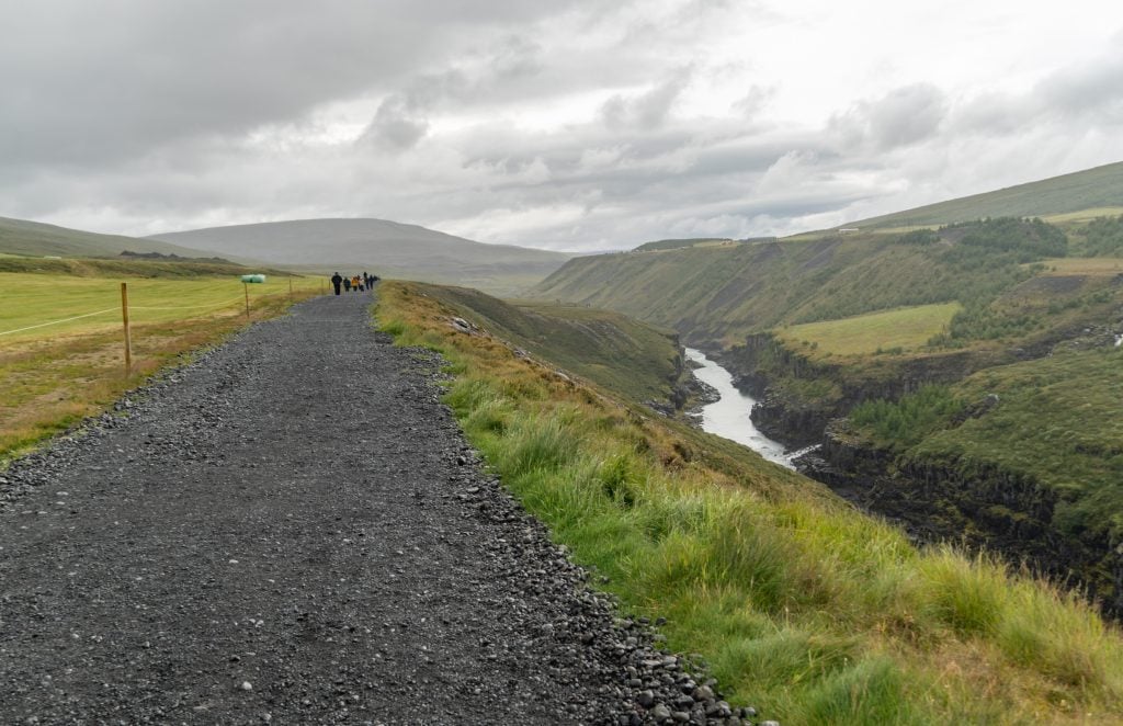 A gravel pathway with hikers passing a river.