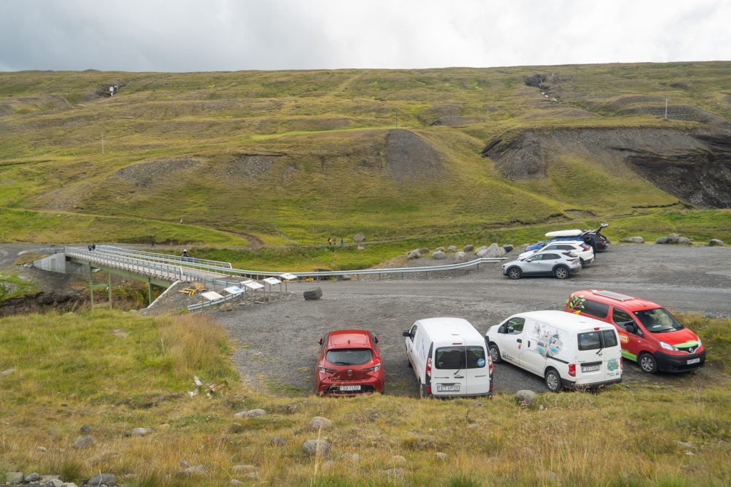 A parking lot next to a river surrounded by grass as far as you can see.