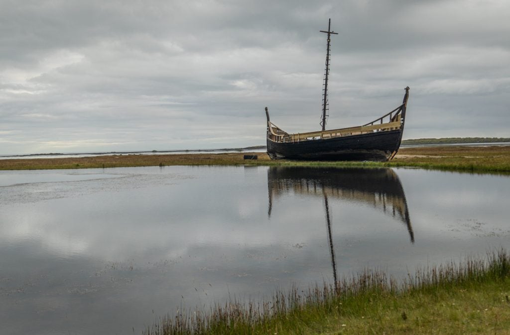 A viking ship docked in still water and reflecting perfectly.
