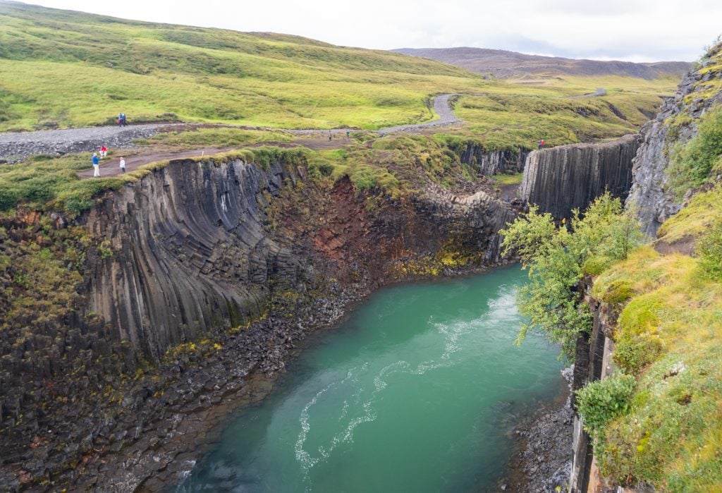 A canyon with a bright turquoise river, lined with long skinny basalt columns.