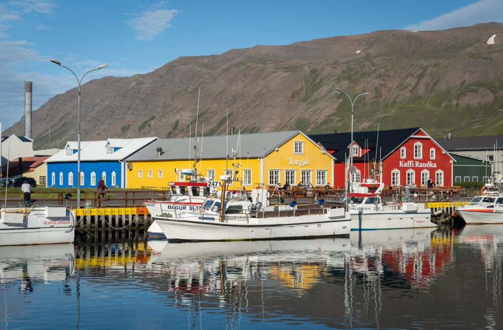 Bright red, yellow, and blue buildings next to a dock with a long white boat.
