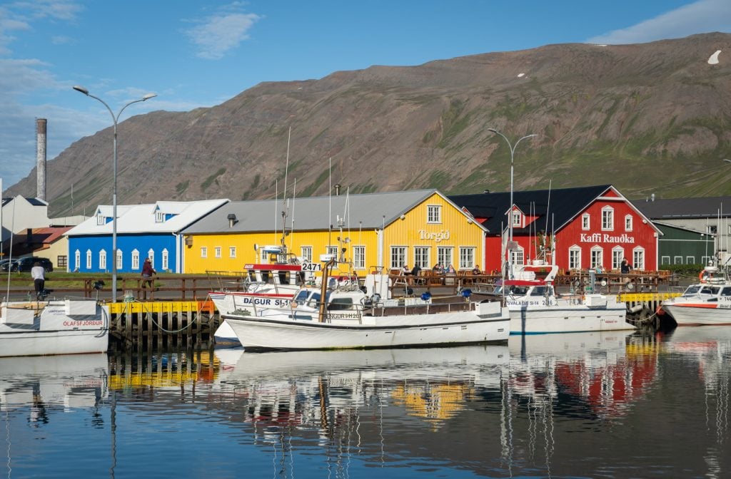 Bright red, yellow, and blue buildings next to a dock with a long white boat.