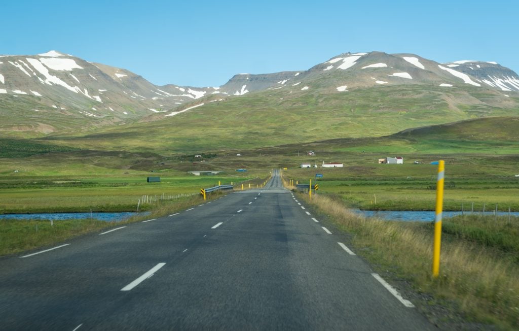 A paved road leading across the river and into snow-topped mountains.