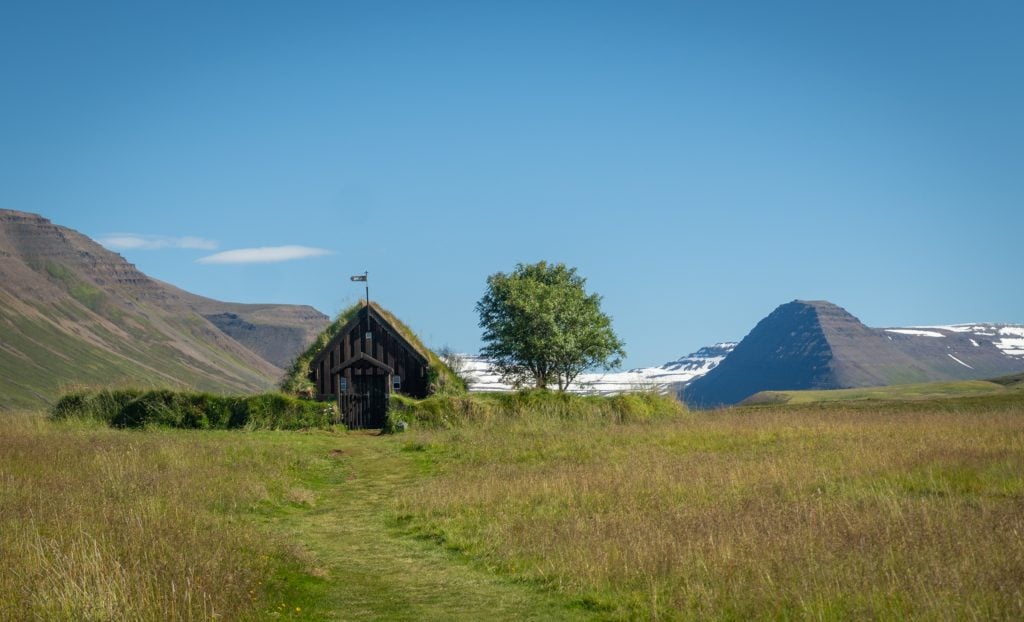 A small triangular church with a grassy roof perched in the middle of a field.