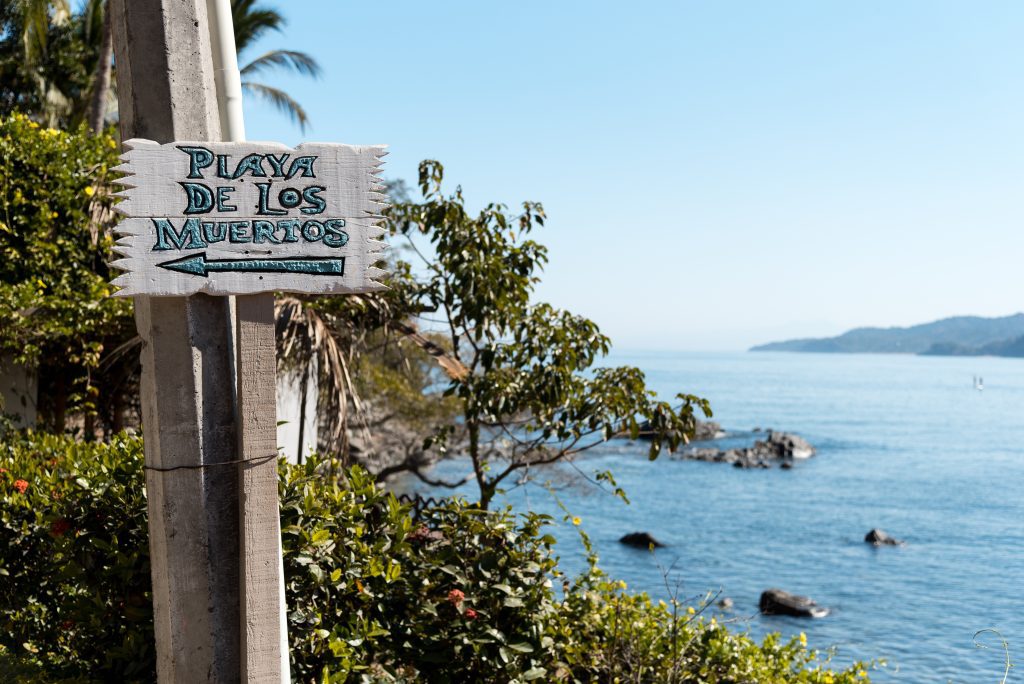 A sign reading "Playa los Muertos" in the jungle near the sea.