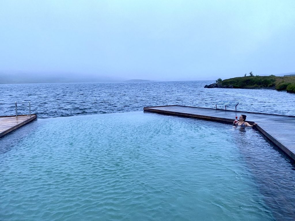 Kate sitting alone in a giant geometric turquoise pool, sipping her slushy.