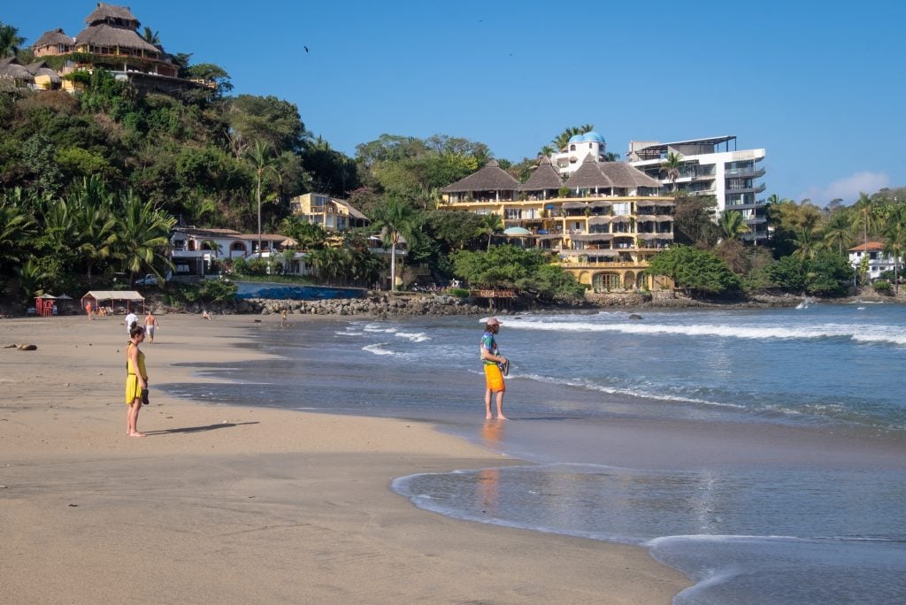 Two people standing in the shallow surf on a beach.