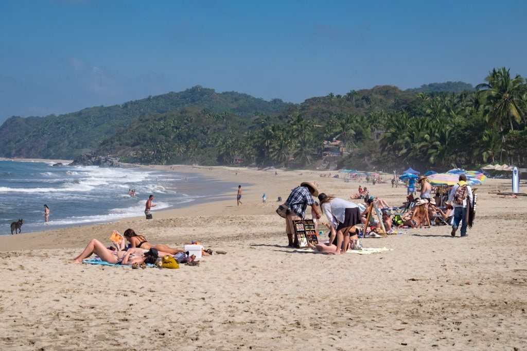 A long stretch of beach with people sunbathing and vendors selling things.