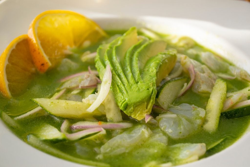 A plate of shrimp aguachile, marinated shrimp swimming in green sauce with chips and avocado