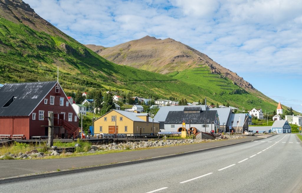 A small town with brightly colored cottages and churches nestled up against a steep green hill.