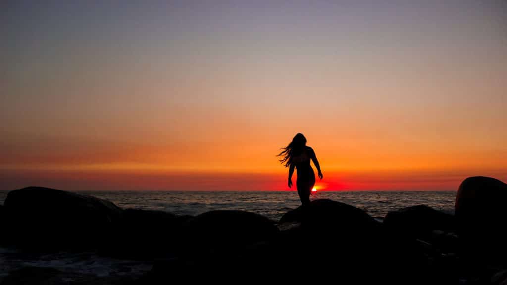 A woman watching a bright red sunset on the beach.