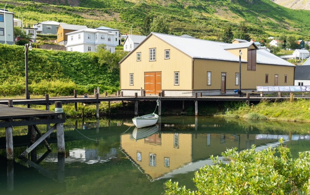 A yellow building perched on top of a green pond with a white canoe reflecting in the water.