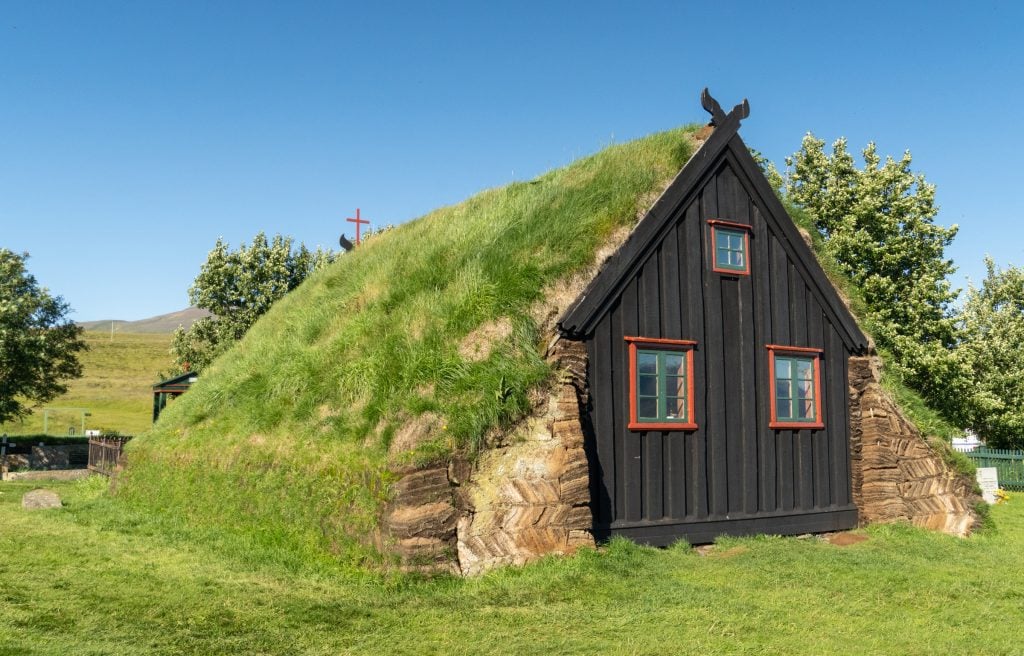 A small triangular wooden church with grassy roofs.