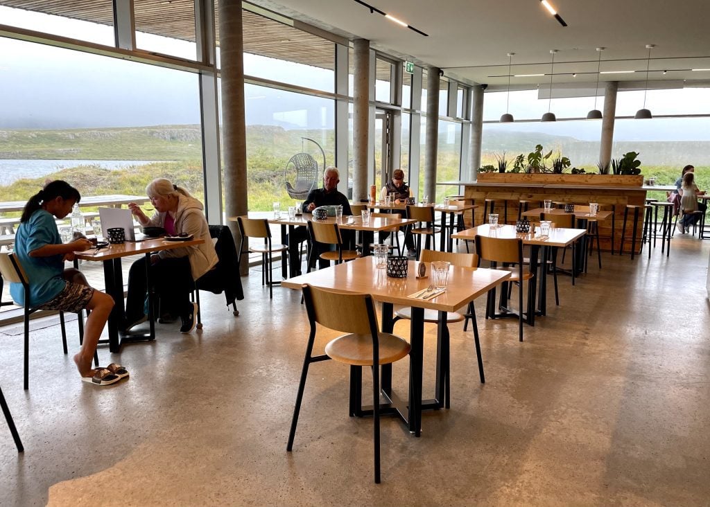 A dining room with floor to ceiling windows and wooden tables and chairs.