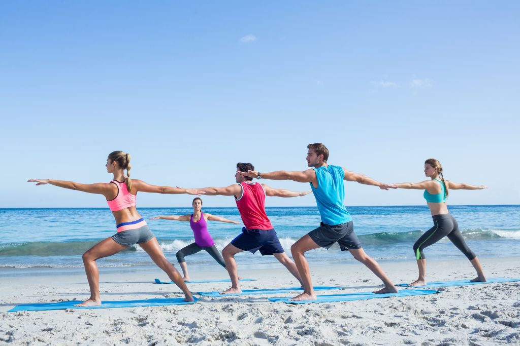 Five people doing yoga on the beach on a sunny day.