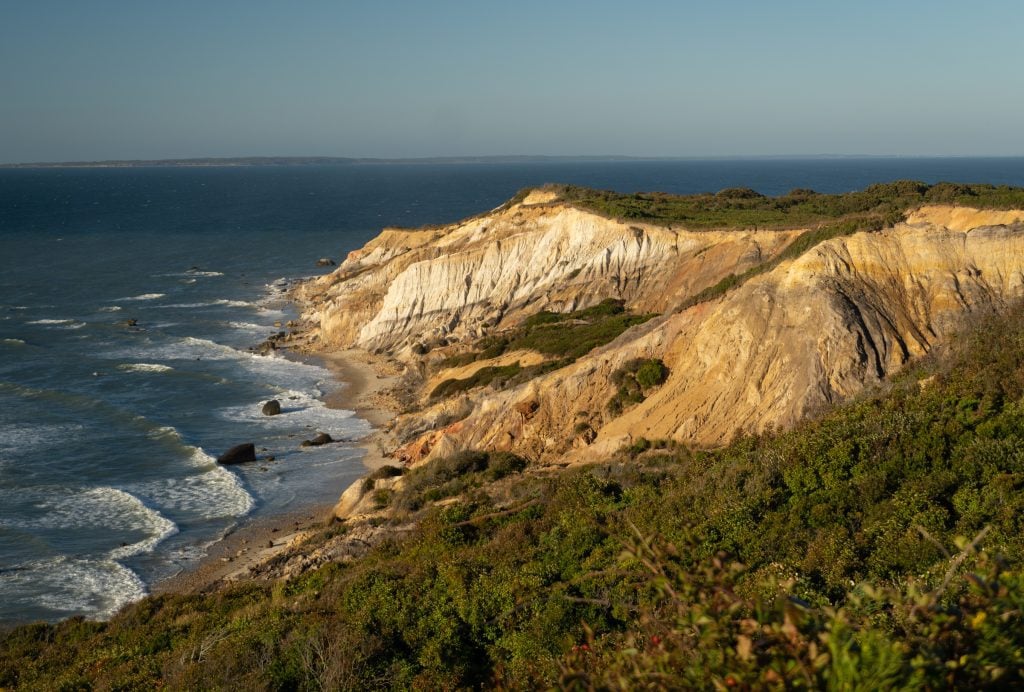 Giant seaside cliffs lit up at sunset in shades of yellow, red, and orange.