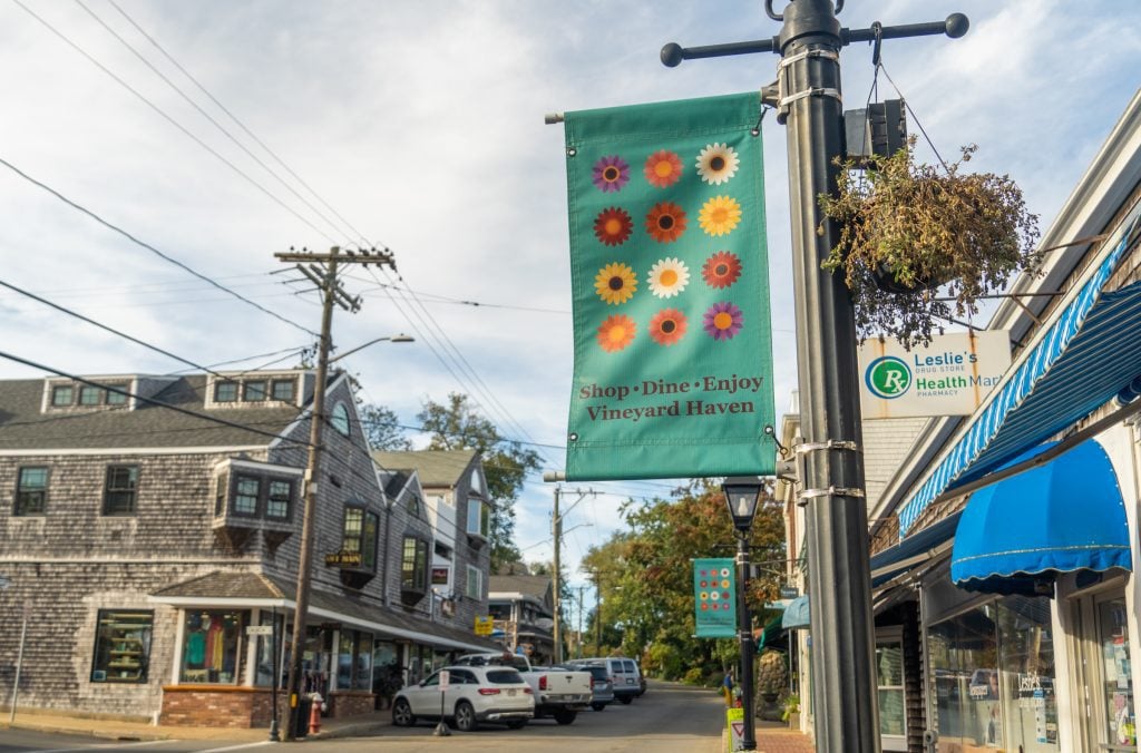 A downtown area with wooden shingled houses and a street sign reading Shop Dine Enjoy Vineyard Haven.