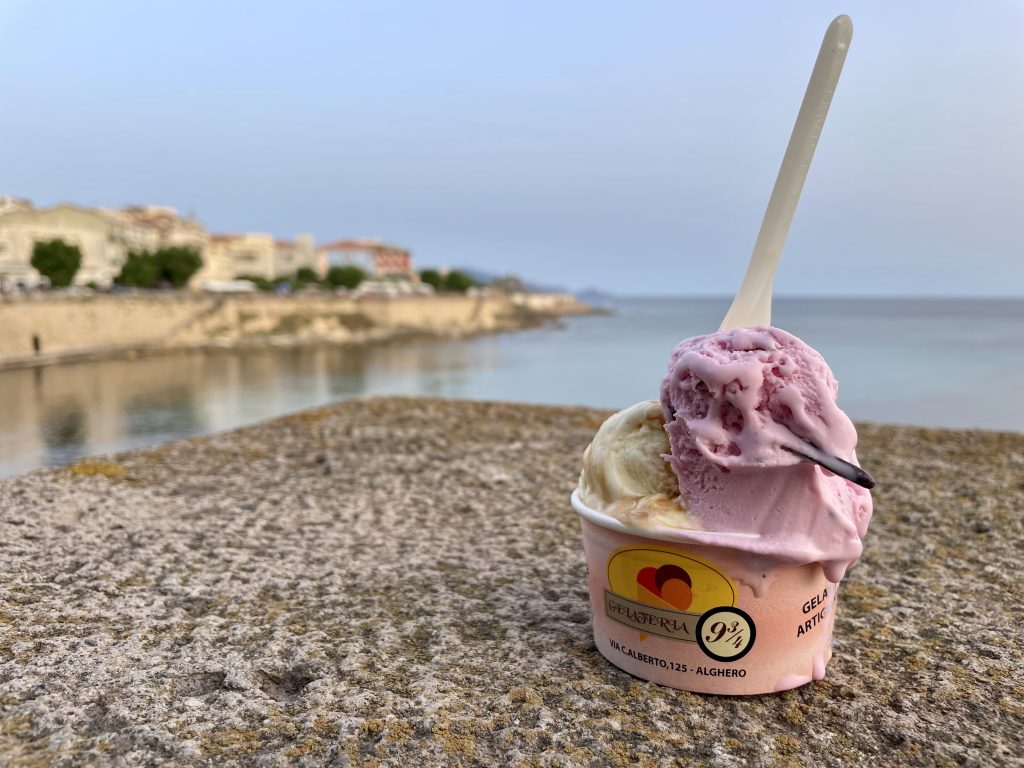 A cup with white and purple ice cream sitting on a table overlooking the calm blue water.