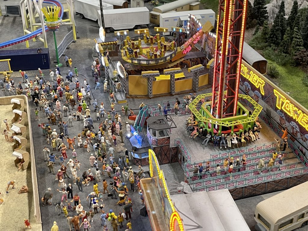 A miniature set of a carnival scene, complete with crowds in front of rides.