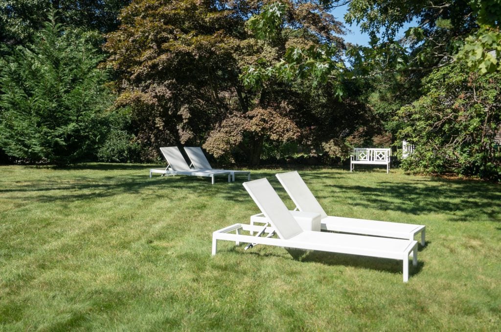 A large green lawn with several white lounge chairs.