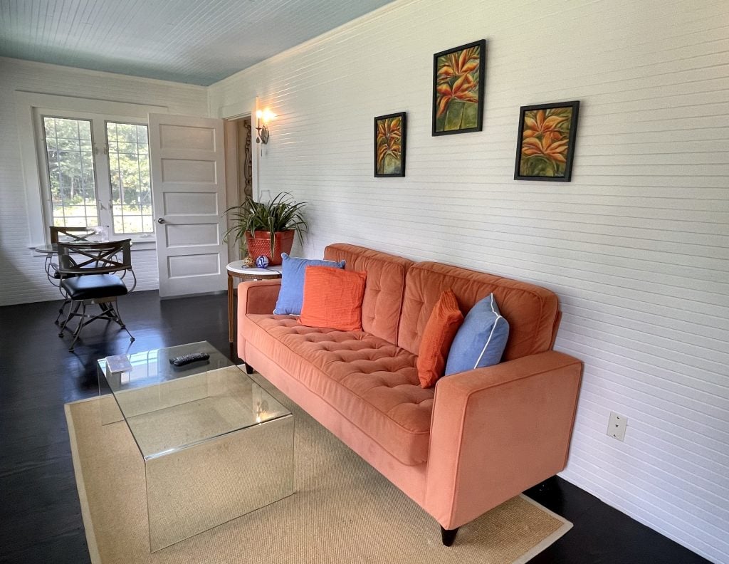 A sitting room with a bright orange couch, small dining table, and lots of light from the windows.