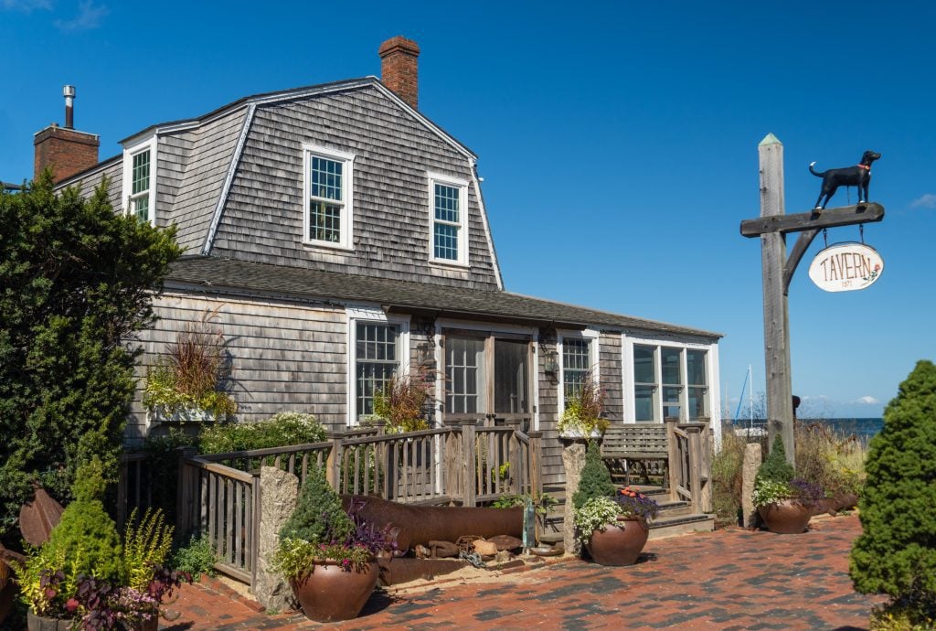 A small house covered with weathered gray shutters and a sign topped with the outline of a black dog.