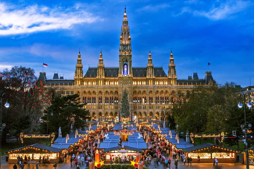 An elegant palace with a stately Christmas market filling the street in front of it.