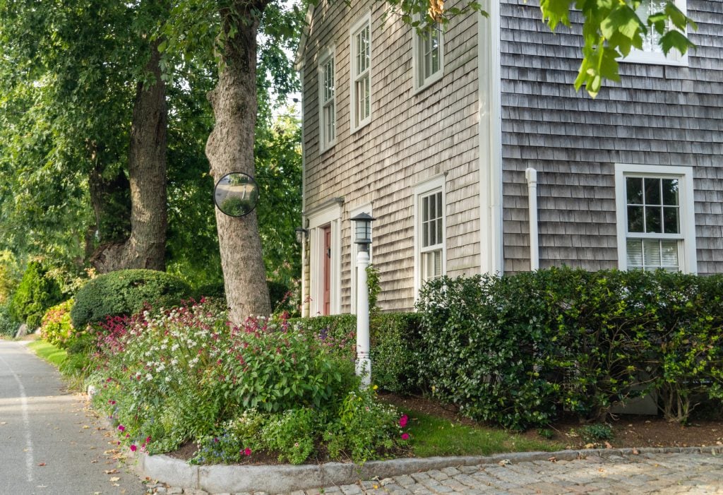 The front of a gray shingled home surrounded by bushes.