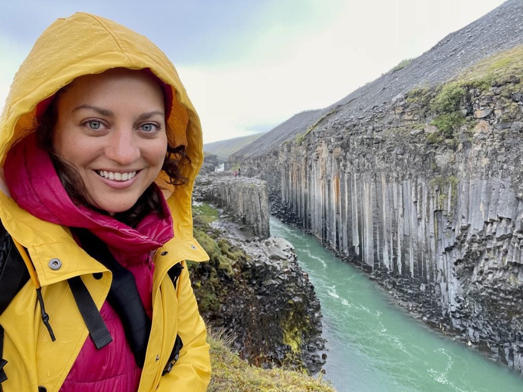 Kate in a bright yellow raincoat over a bright pink coat, standing in front of a canyon of tall thin rock columns.