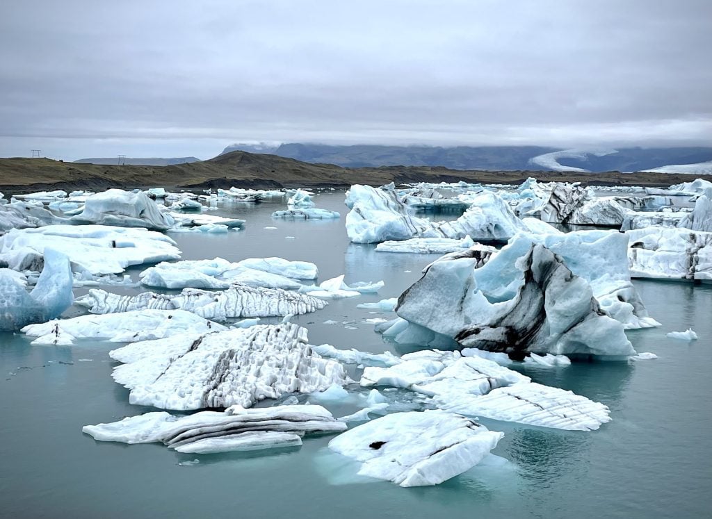A still lagoon filled with floating icebergs on a cloudy day.