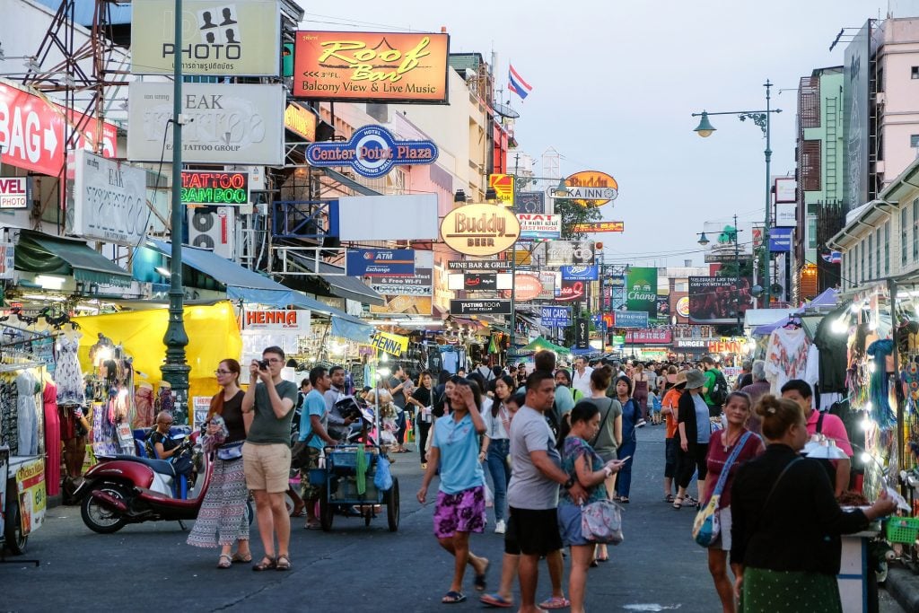 Crowds of Backpackers walking down a busy Khao San Road, filled with bars.