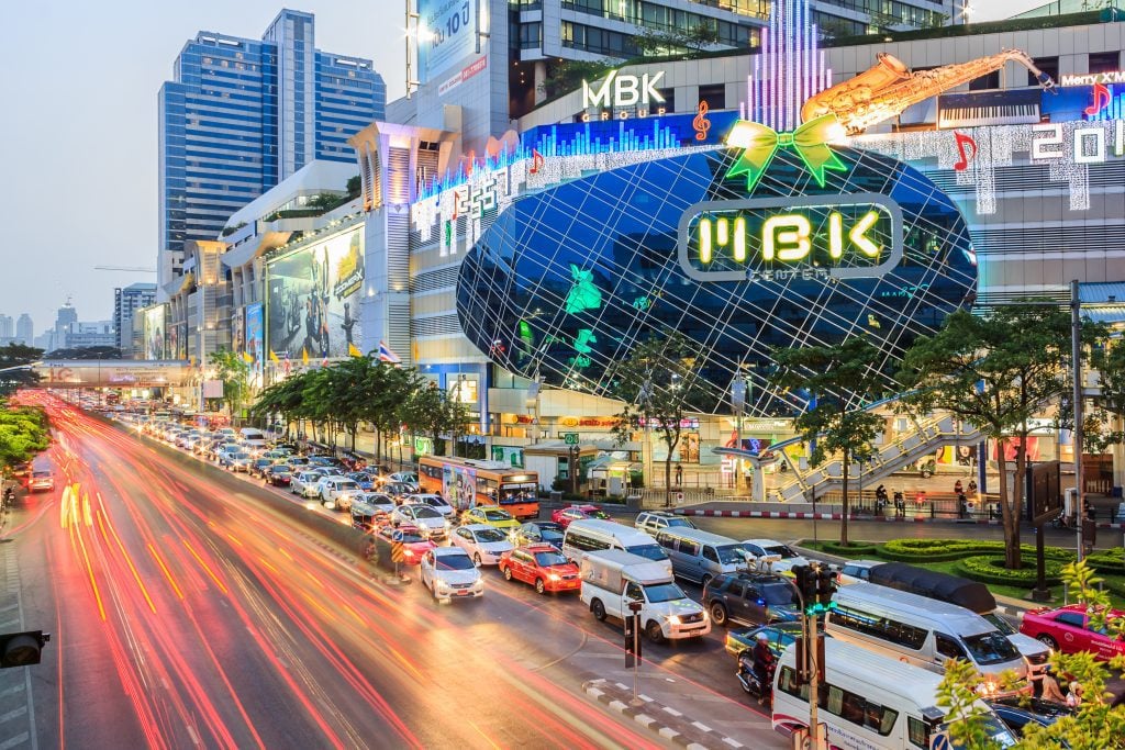 MBK shopping center next to a traffic-filled street in Bangkok, lit up at sunset.