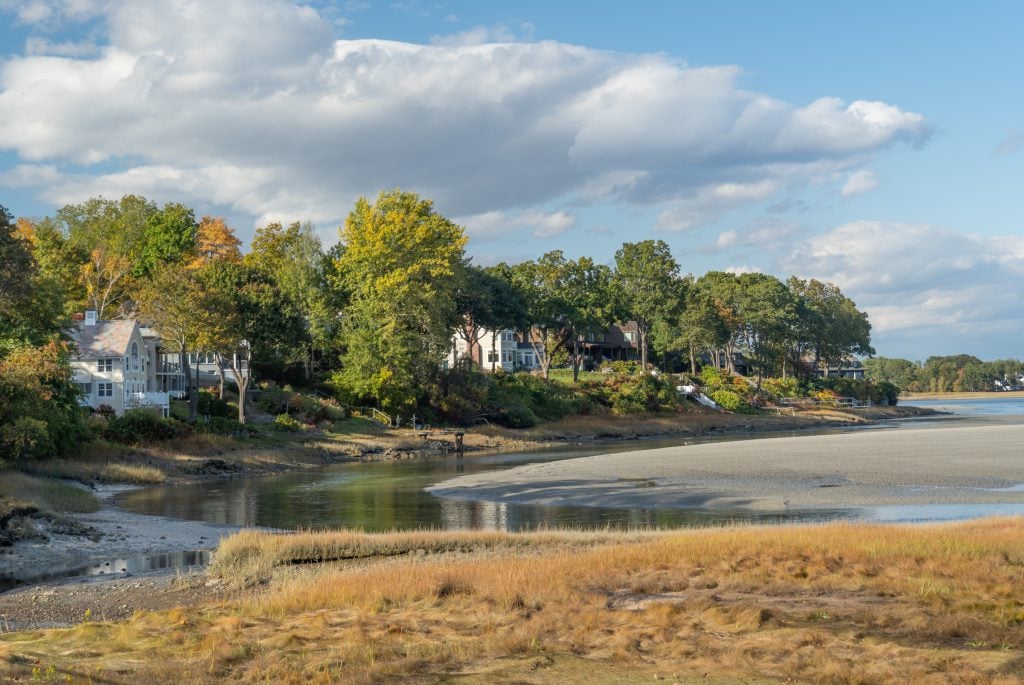 A marshy area in front of a beach, with lots of big houses perched on shore.