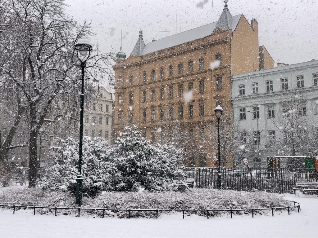 A big snowstorm in a park in Prague, a crenellated yellow building in the background.