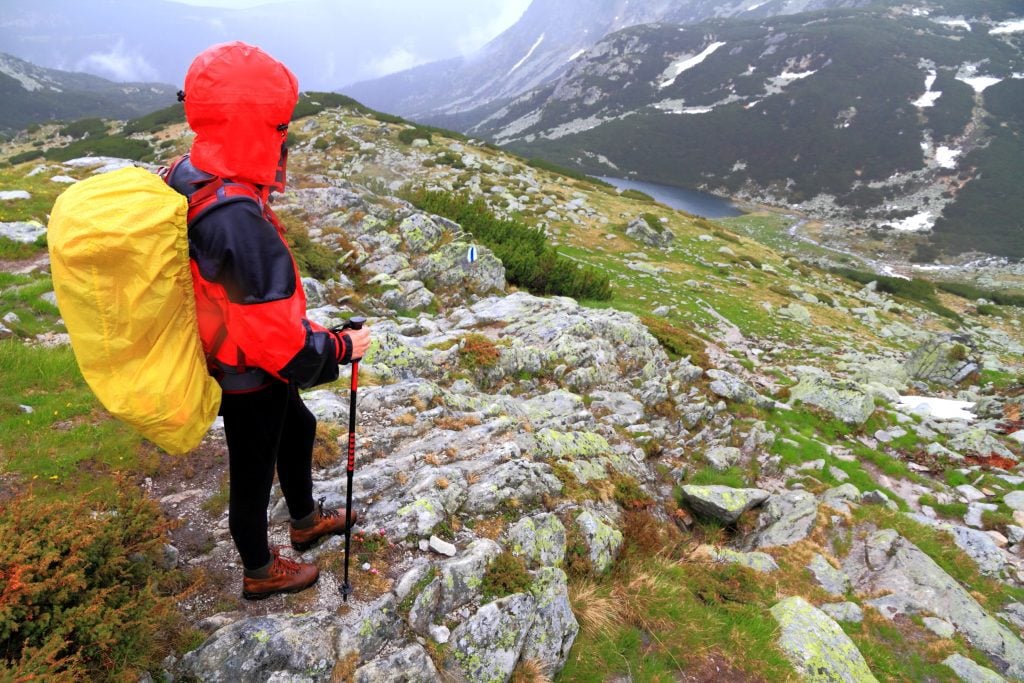 A hiker looking over a canyon, wearing a big backpack with a bright yellow waterproof cover over it.