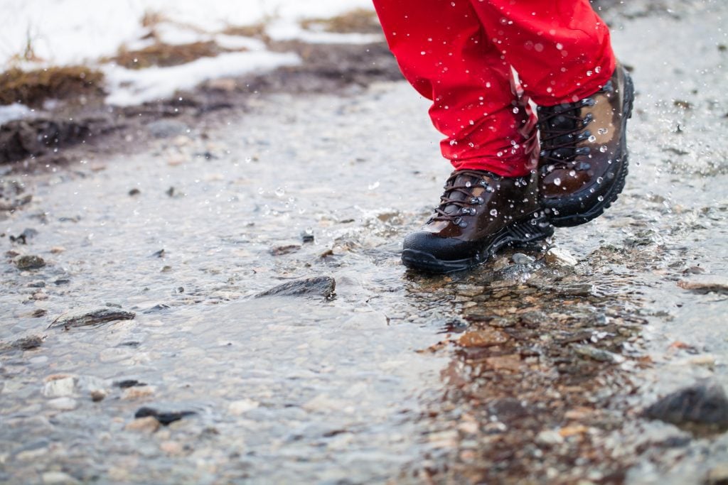 A person's feet in hiking boots walking through a wet path.