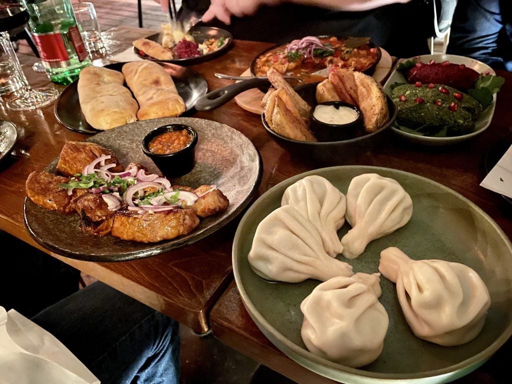 A table full of Georgian food: kinkhali soup dumplings, stewed chicken, walnut and beet dips, a boat-shaped khachapuri, and pork shashlik.
