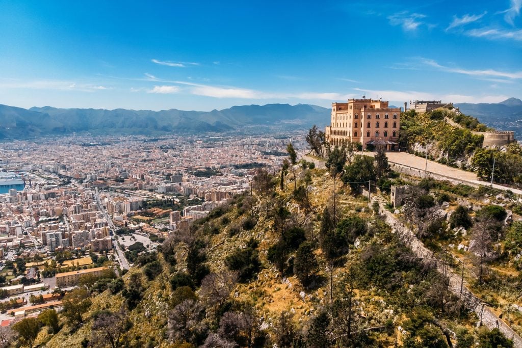 A church atop a hill overlooking a city surrounded by mountains.