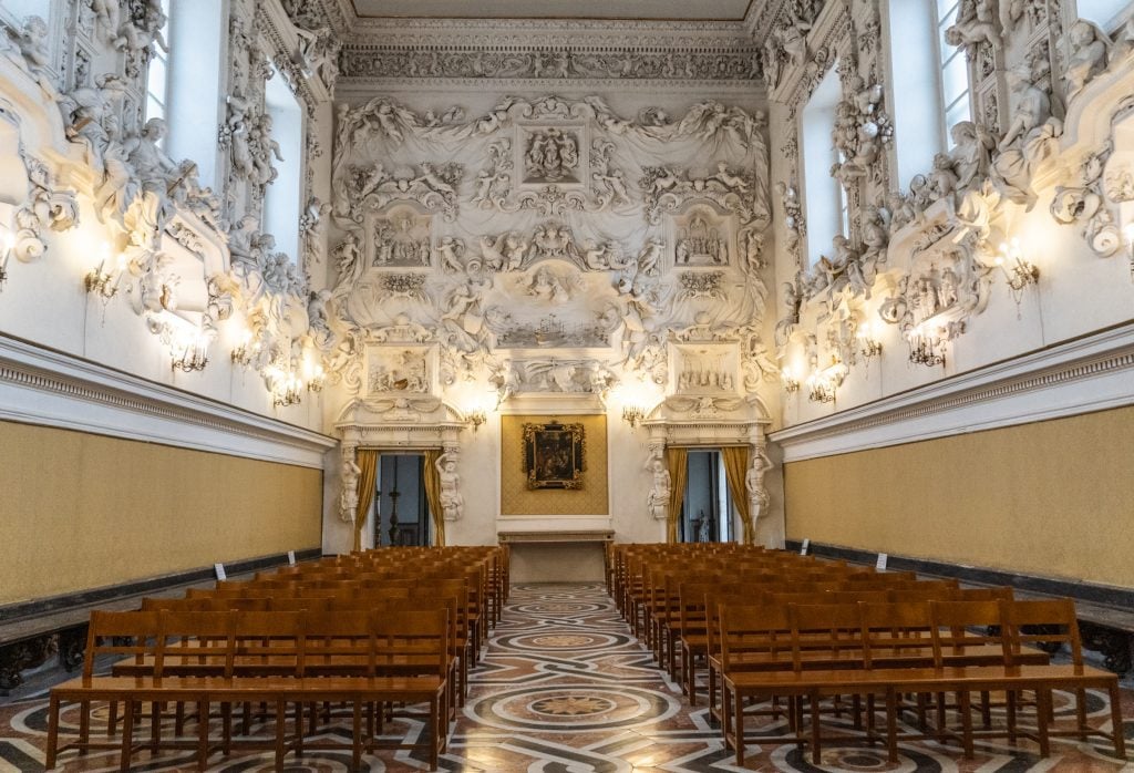 A very small chapel. The top half of the walls is covered with intricate sculpture work of angels and demons, all in white stucco.