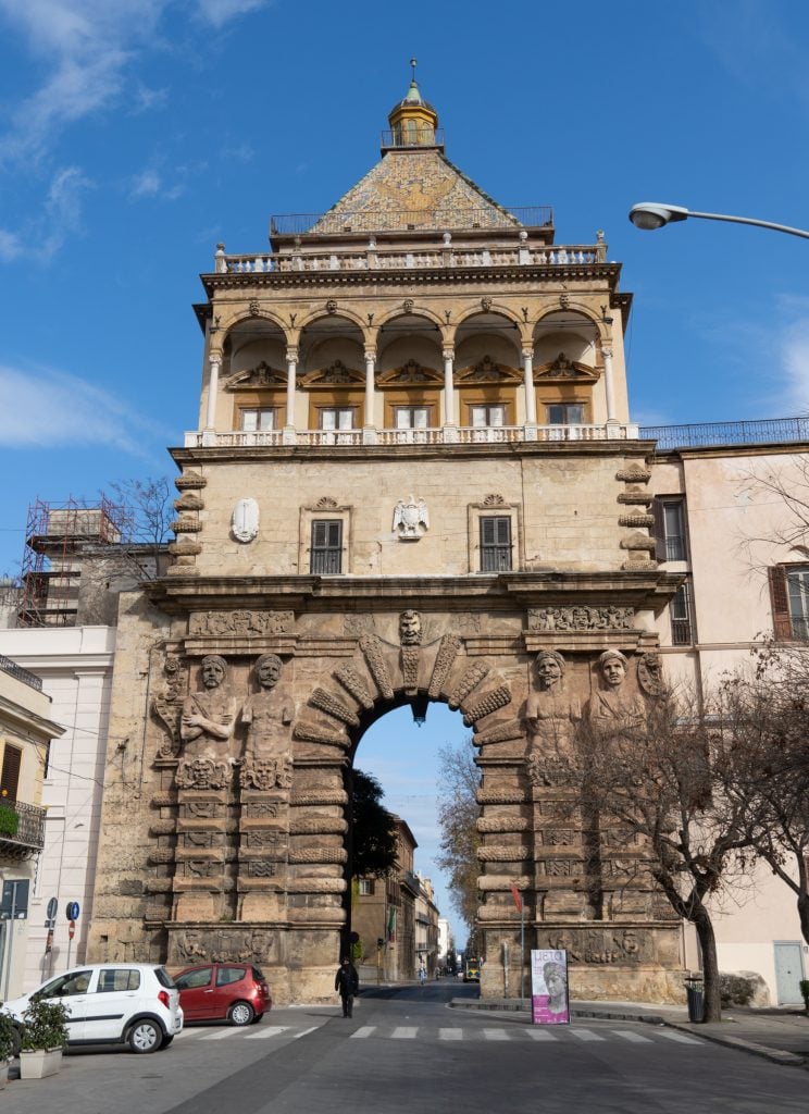 A three-story gate. The bottom is all stone blocks and has a narrow opening, but the top has a balcony, a mosaic roof, and intricately cut porticoes.